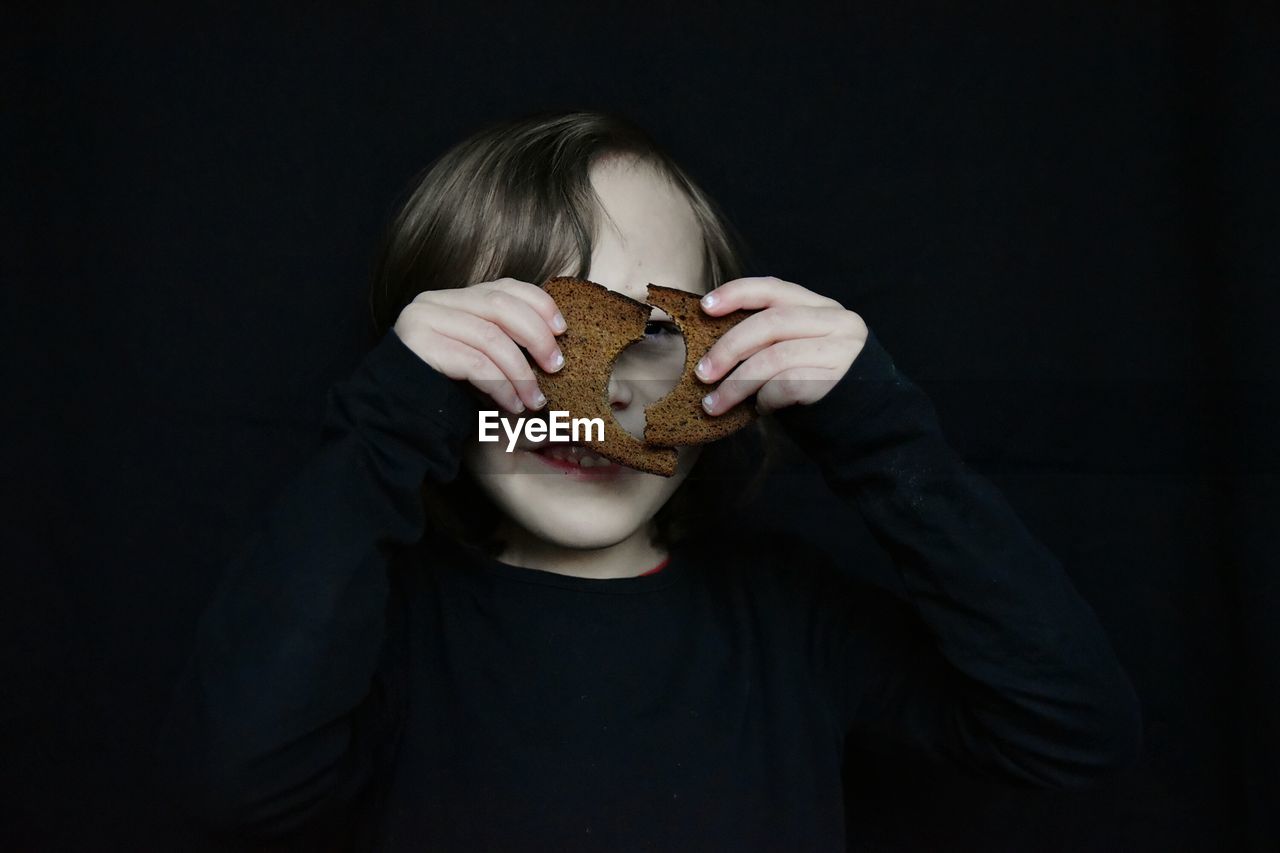 Close-up of girl holding bread against black background