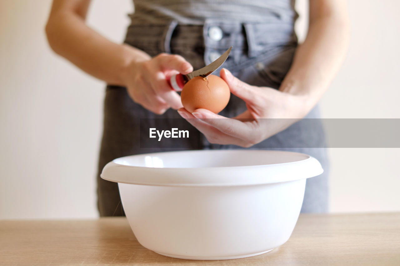 Woman breaks an egg with a knife over a plate to cook a delicious meal