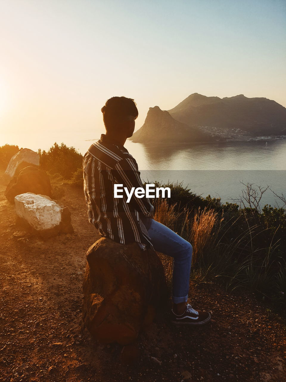 MAN SITTING ON ROCK LOOKING AT VIEW OF MOUNTAIN