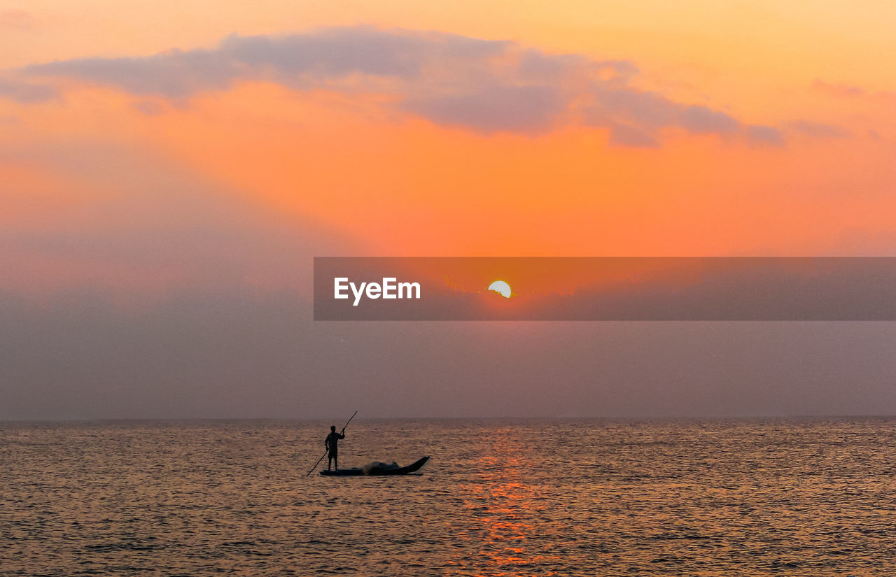 Silhouette person in sea against sky during sunset