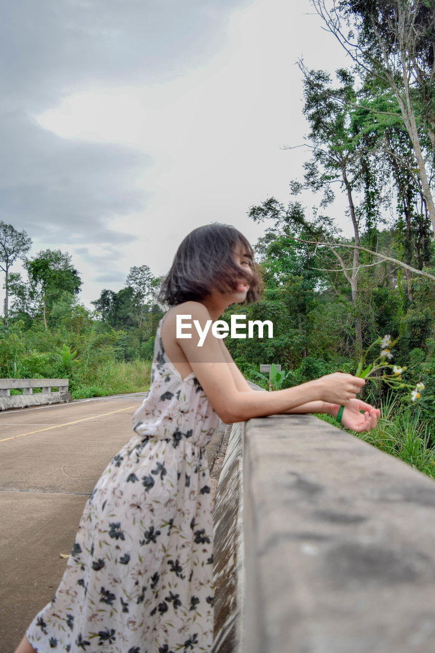 Side view of young woman standing by road against sky