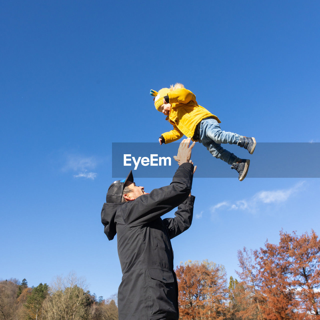 low angle view of man with arms outstretched standing against clear blue sky