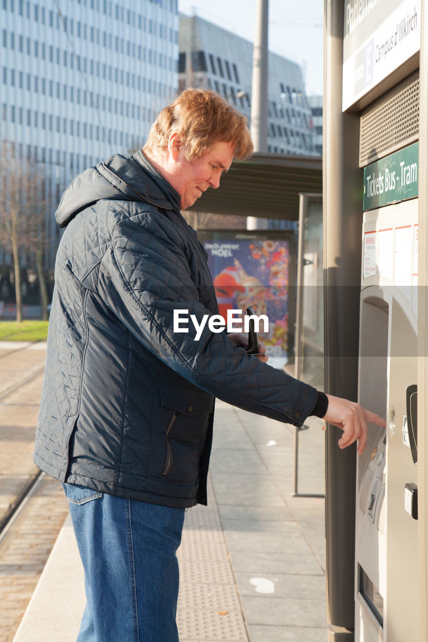 SIDE VIEW OF MAN STANDING BY TEXT ON CITY STREET