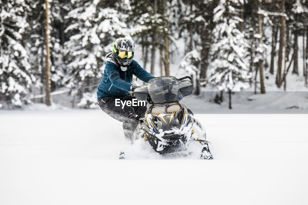Skilled snowmobiler stands on side, preparing for powder turn.