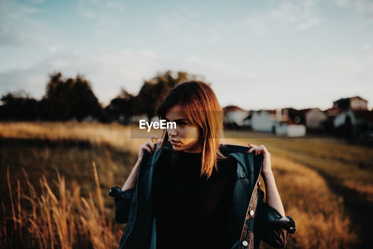 BEAUTIFUL WOMAN STANDING ON FIELD AGAINST SKY AT SUNSET