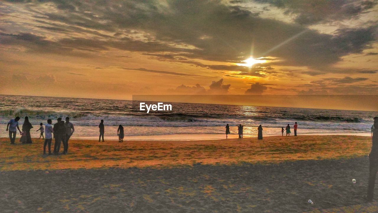 PEOPLE ON BEACH AGAINST SKY AT SUNSET