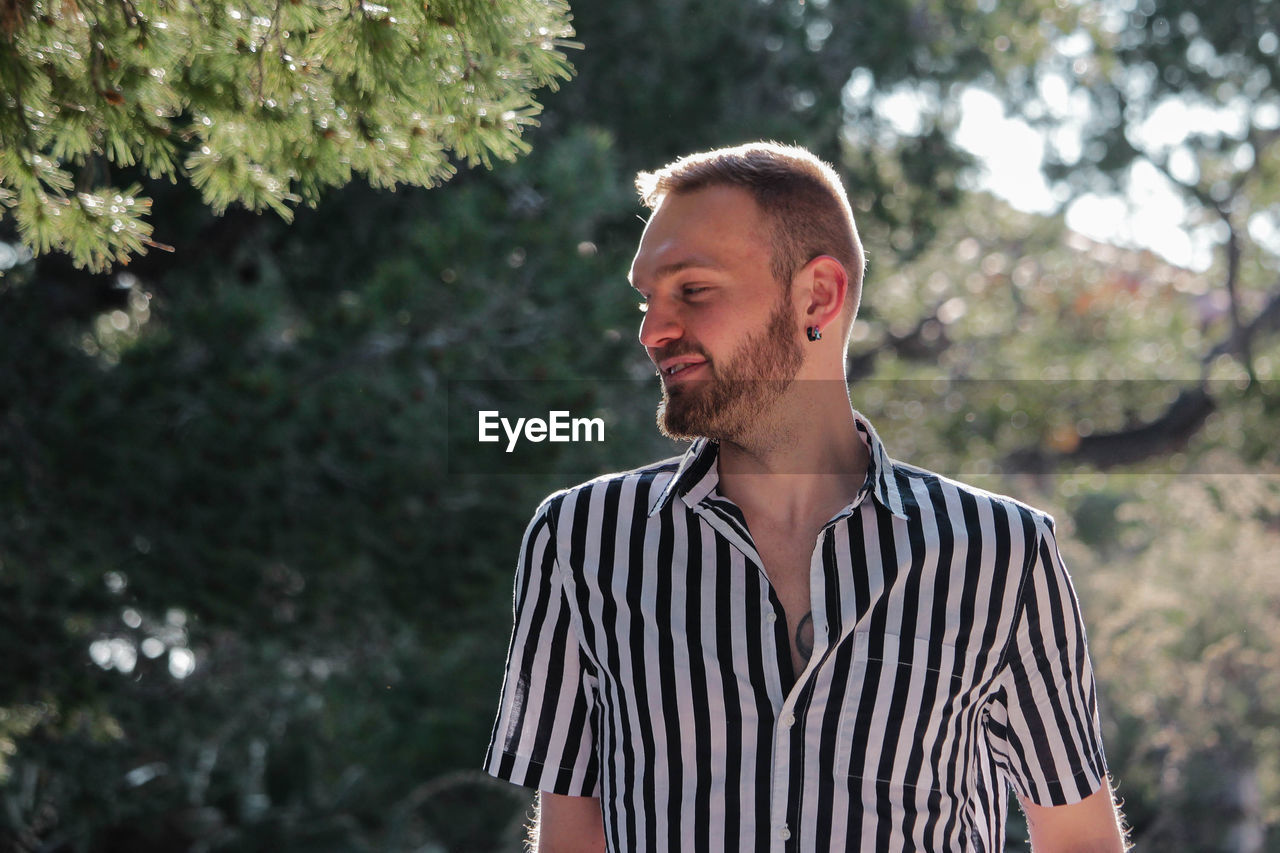 Handsome man wearing striped shirt against trees