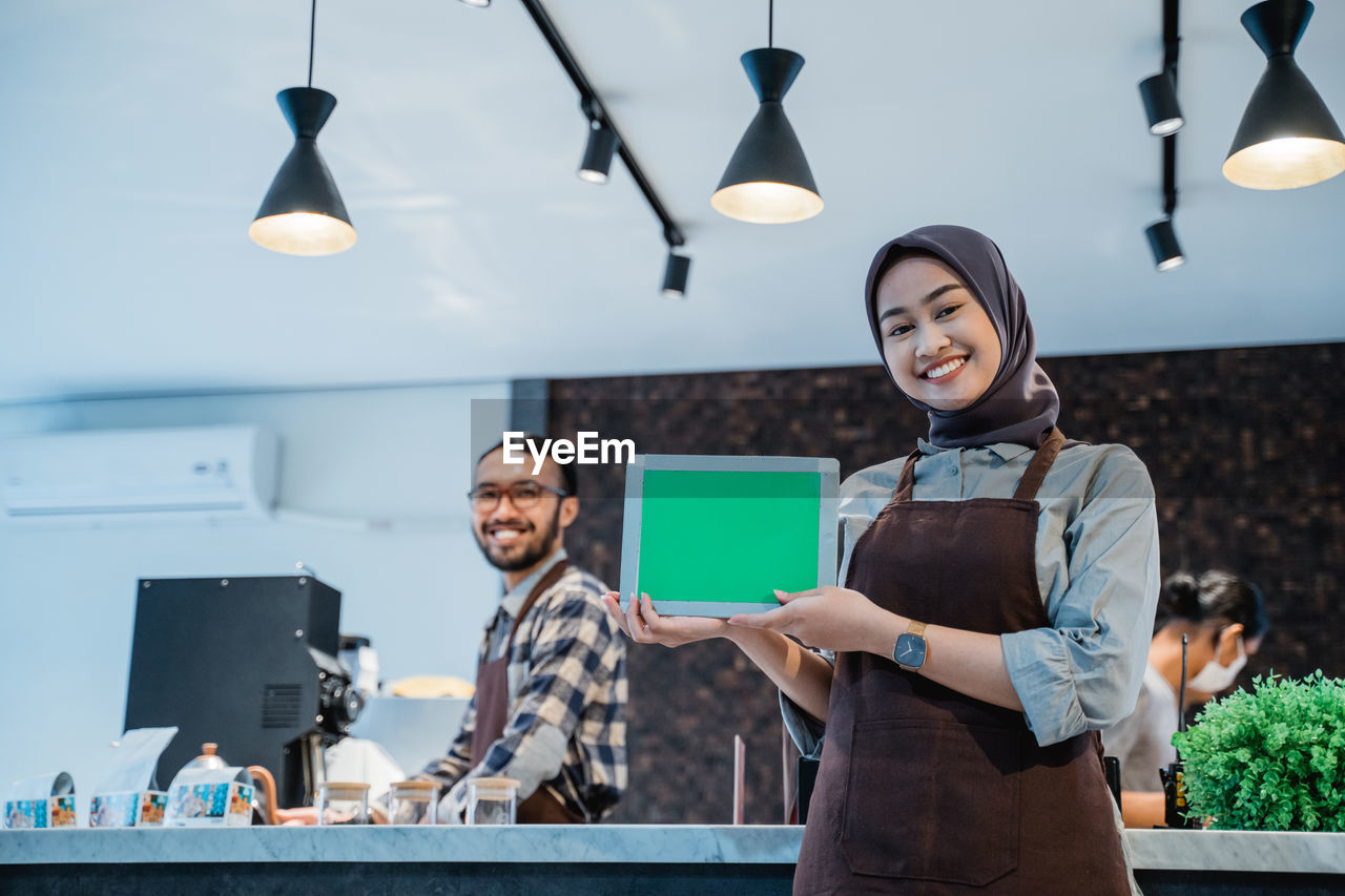 portrait of smiling young woman using digital tablet while standing against wall