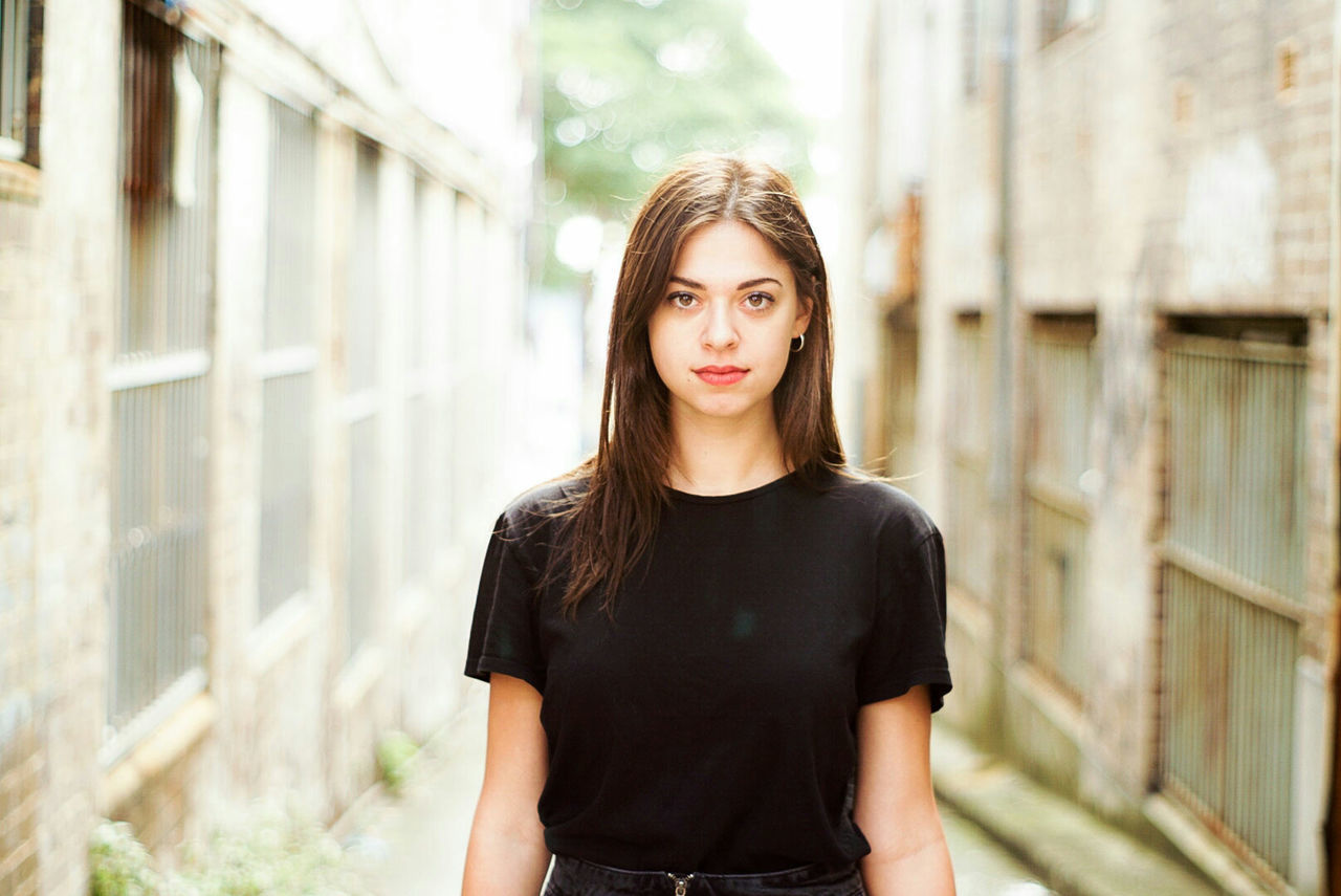 PORTRAIT OF YOUNG WOMAN STANDING AGAINST WALL