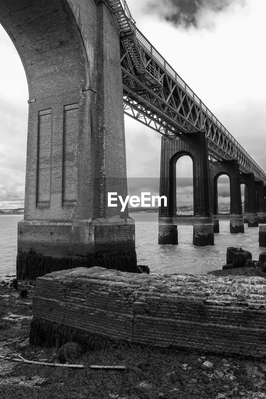 Low angle view of bridge over river against cloudy sky