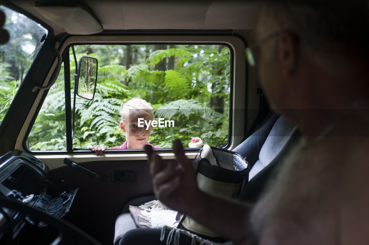 Portrait of man sitting in car while girl standing at window