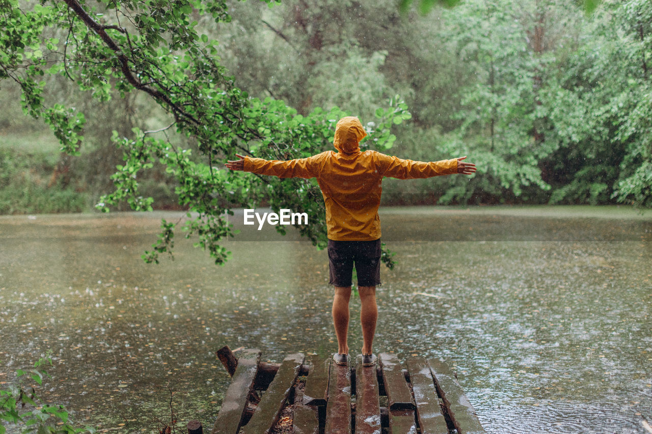 REAR VIEW OF MAN STANDING BY TREE IN LAKE DURING RAINY SEASON