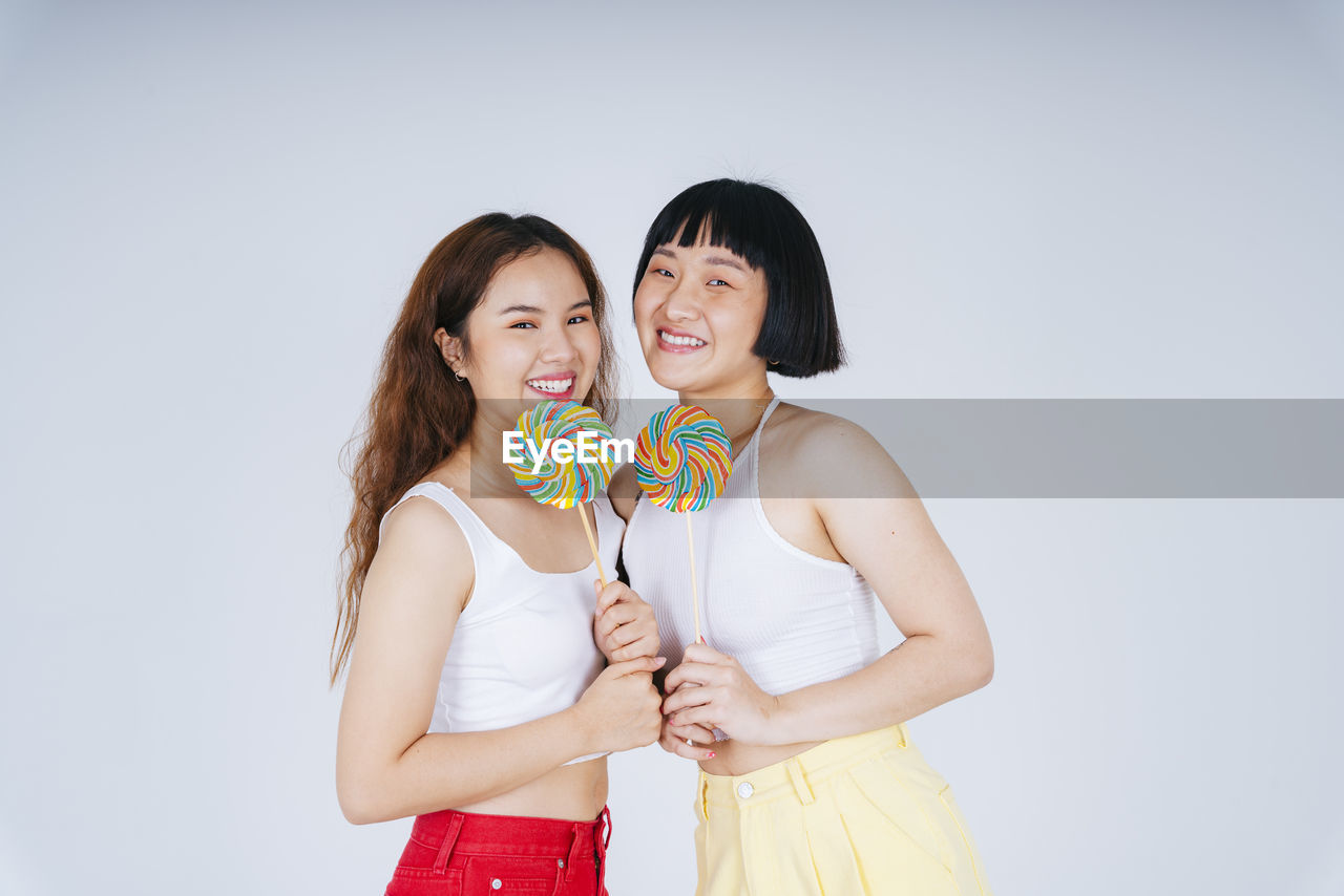 Lesbian couple holding lollipop against white background