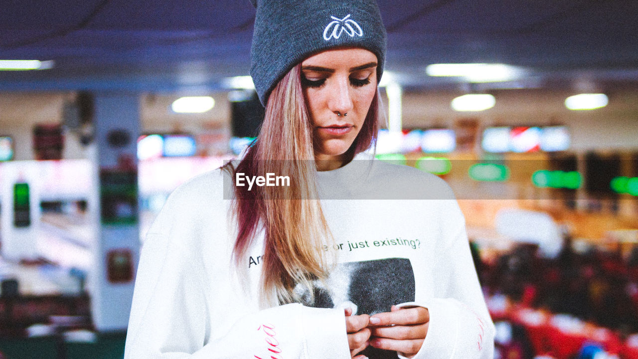 CLOSE-UP OF YOUNG WOMAN HOLDING CAMERA WHILE STANDING IN OFFICE