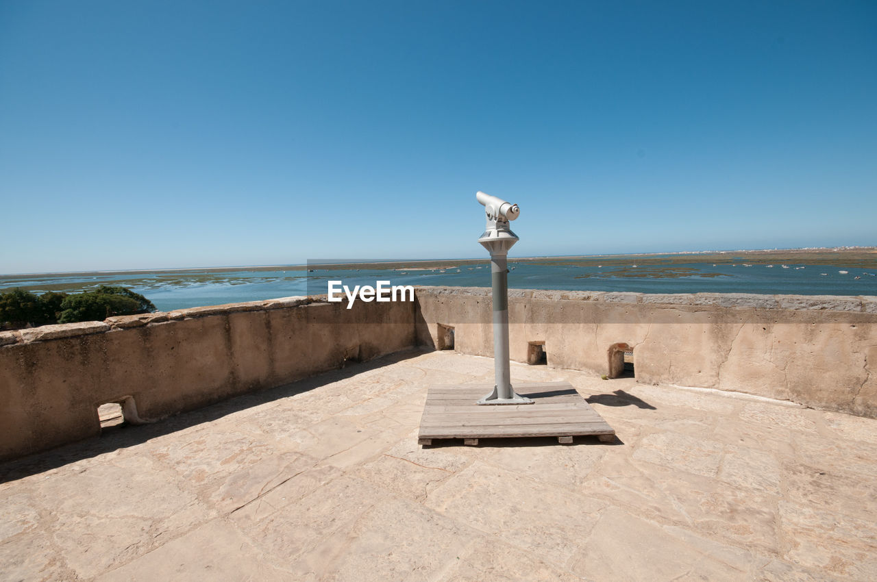 Coin-operated binoculars pointing towards sea against clear blue sky