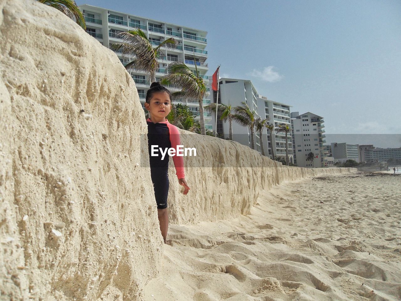 Portrait of girl standing by retaining wall at sandy beach