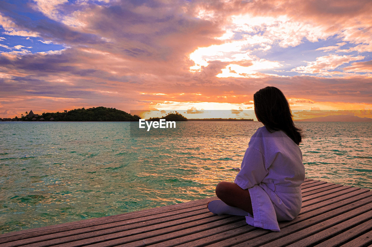 water, sky, sunset, one person, relaxation, sea, nature, adult, vacation, beauty in nature, trip, women, sitting, holiday, horizon, tranquility, cloud, scenics - nature, lifestyles, leisure activity, tranquil scene, sunlight, land, ocean, zen-like, beach, travel destinations, travel, rear view, looking at view, meditating, idyllic, shore, summer, female, solitude, outdoors, environment, contemplation, full length, exercising, dusk, hairstyle, yoga, wellbeing, landscape, long hair, spirituality, evening, sun, young adult, tourism, religion, pier