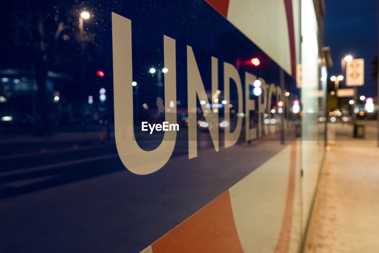 CLOSE-UP OF ILLUMINATED ROAD SIGN ON STREET AT NIGHT