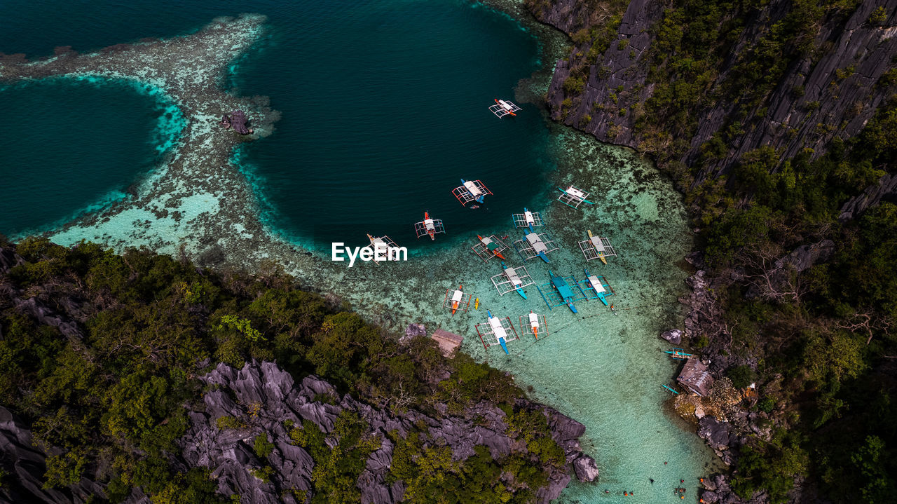 In the photo, a vibrant tropical boat near a beautiful beach or rocky shore.