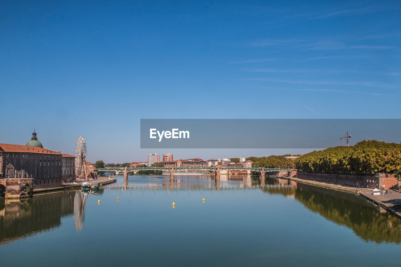Bridge over river by buildings against blue sky