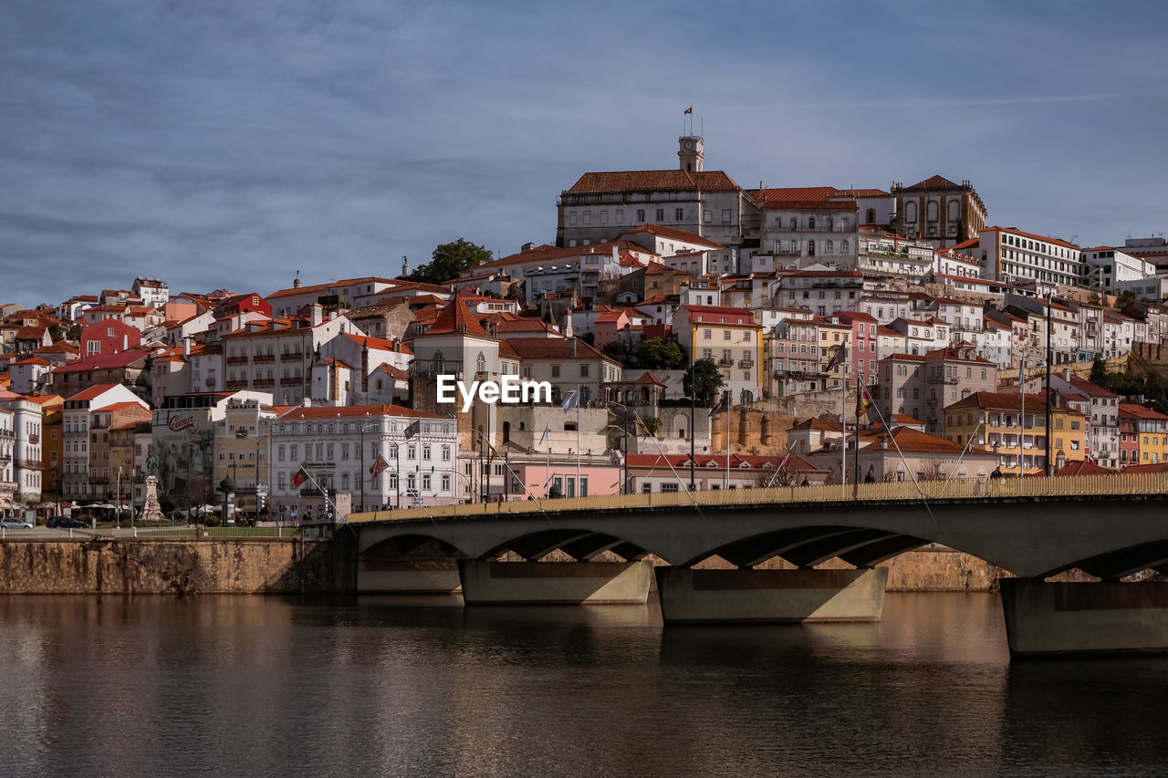 Bridge over river by buildings in town against sky