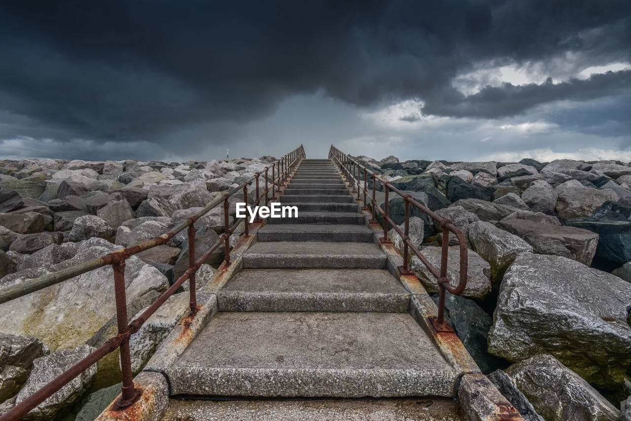 Staircase amidst rocks against cloudy sky