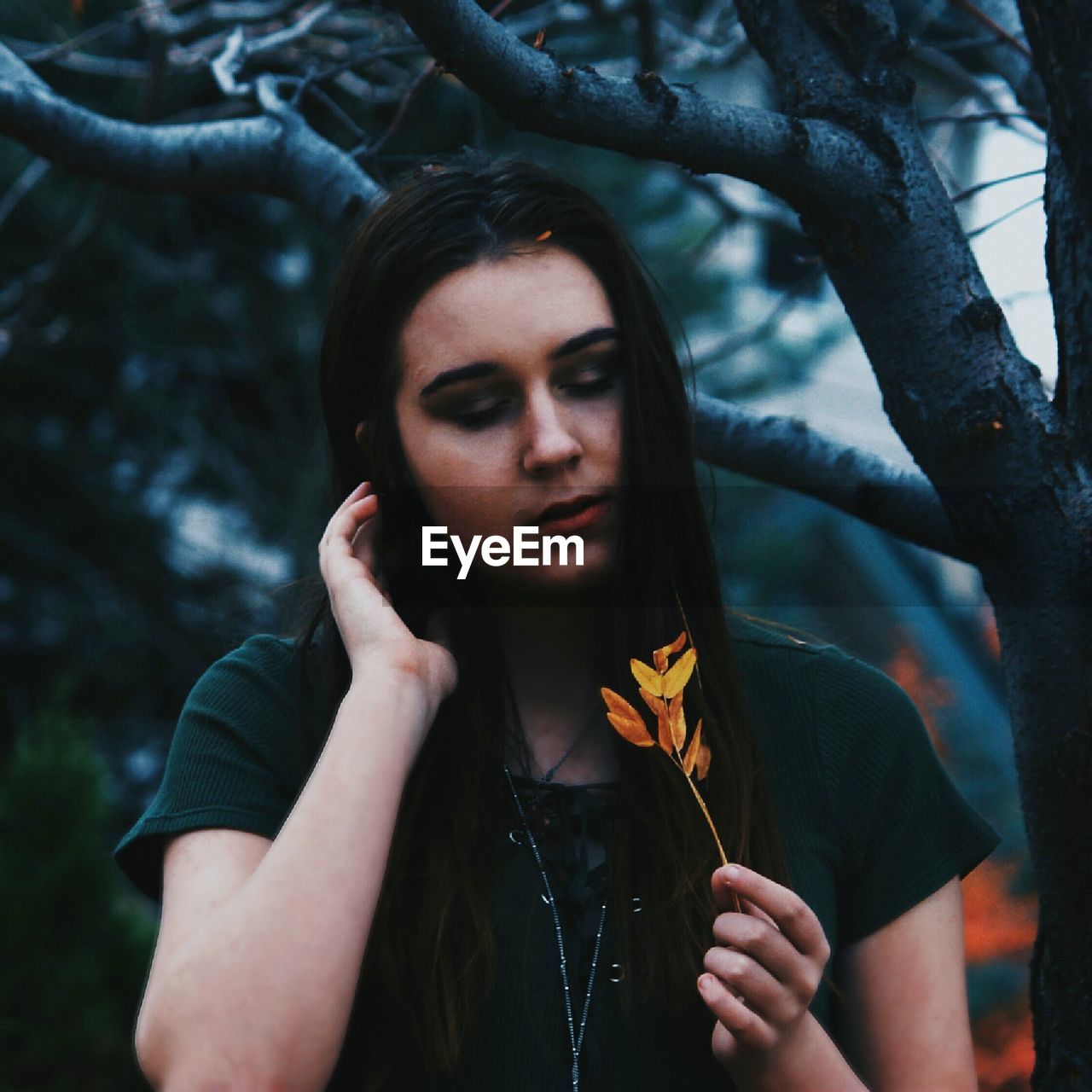 YOUNG WOMAN HOLDING A TREE AGAINST BLURRED BACKGROUND