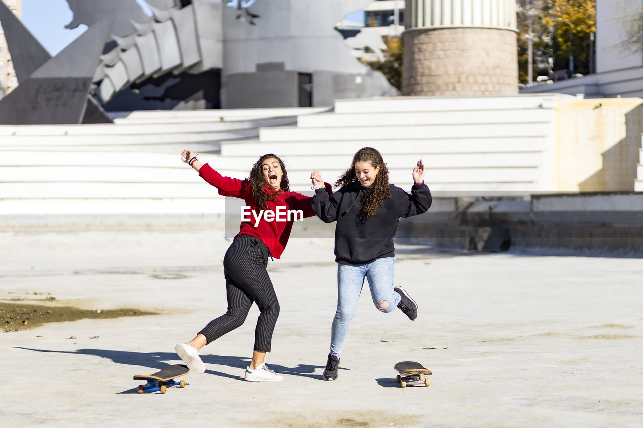 Playful female friends enjoying with skateboard outdoors