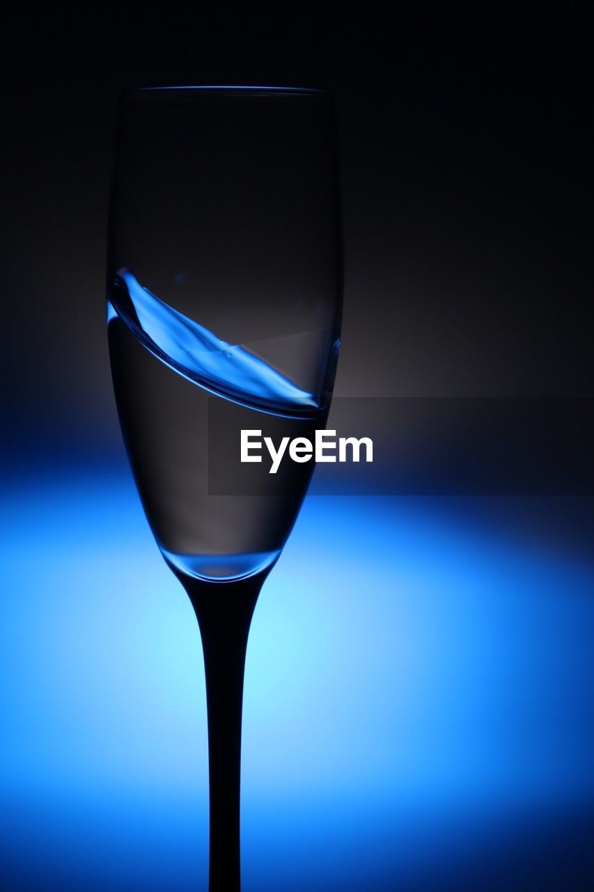 Close-up of champagne flute against illuminated blue light bulb