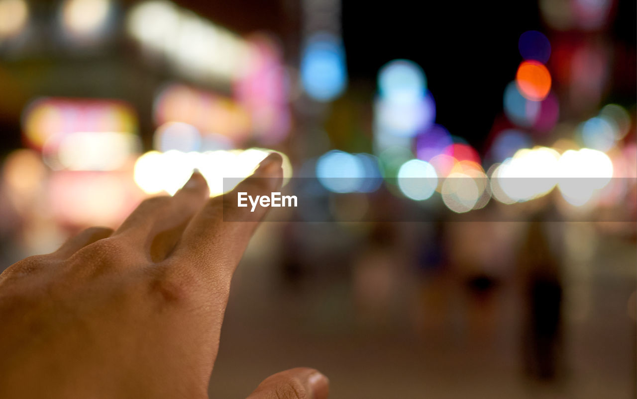 CLOSE-UP OF HAND TOUCHING ILLUMINATED STREET