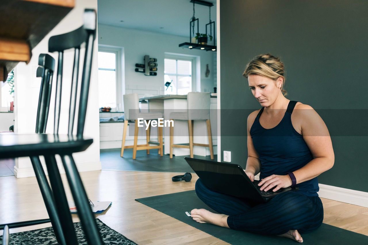 Woman working over laptop while sitting on mat in living room at home