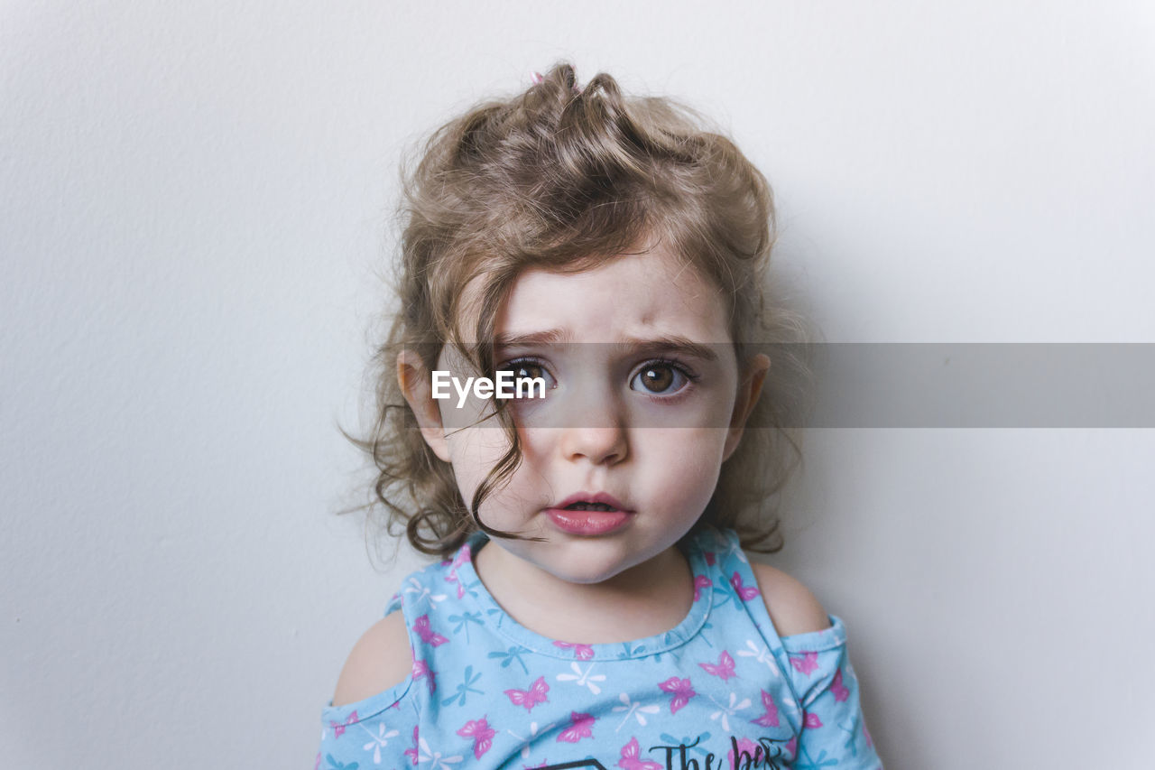 Portrait of cute sad girl against white background