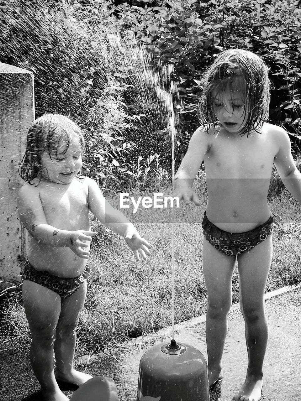 Full length of happy shirtless sisters playing in sprinkler on street