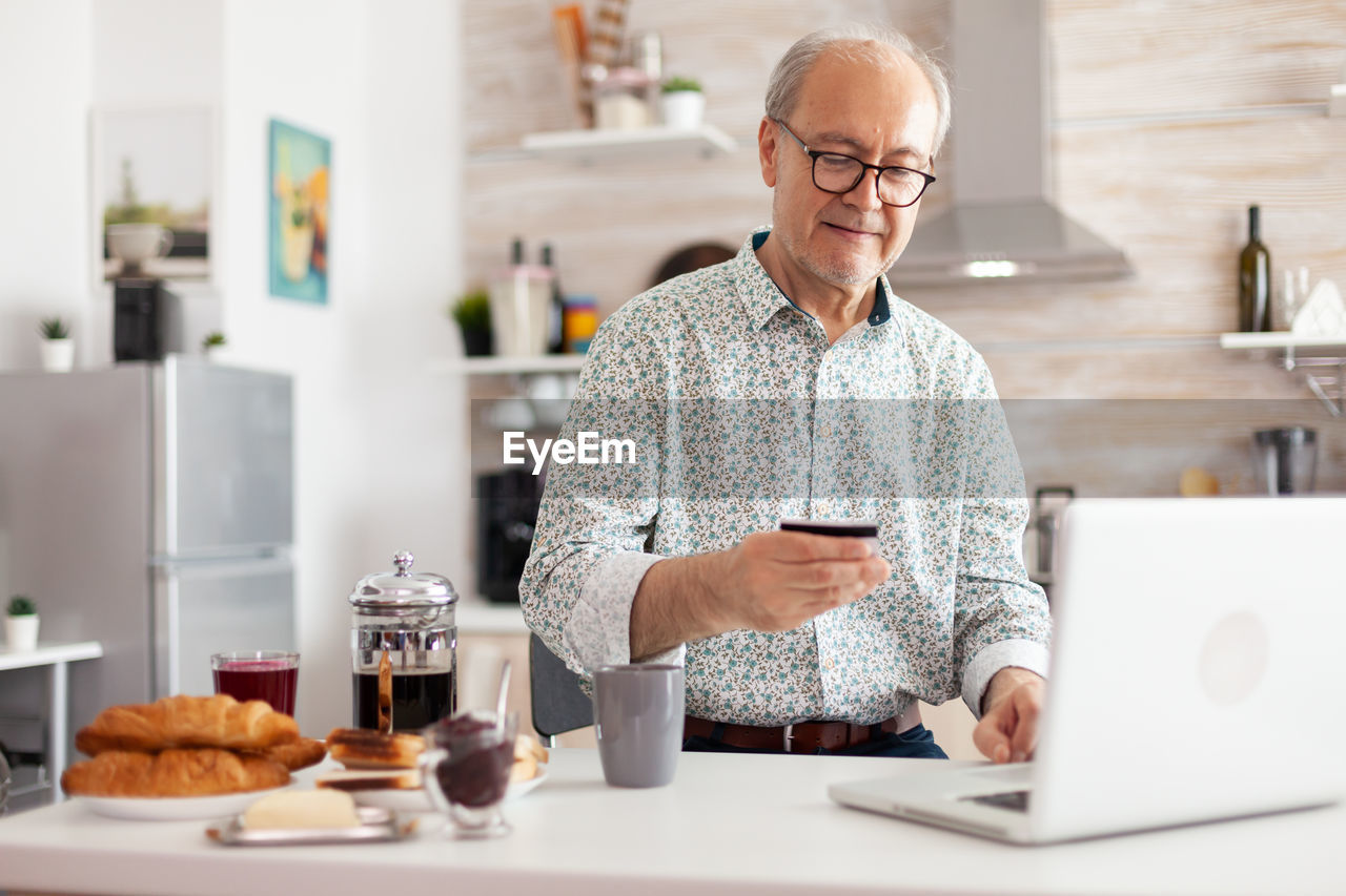 Senior man holding credit card while using laptop at home