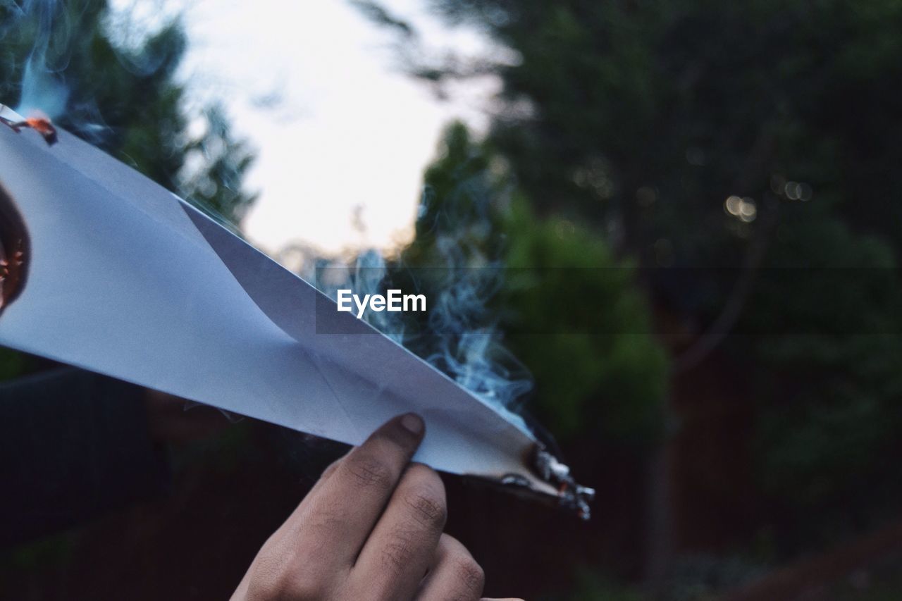 Cropped image of hand holding burning paper plane