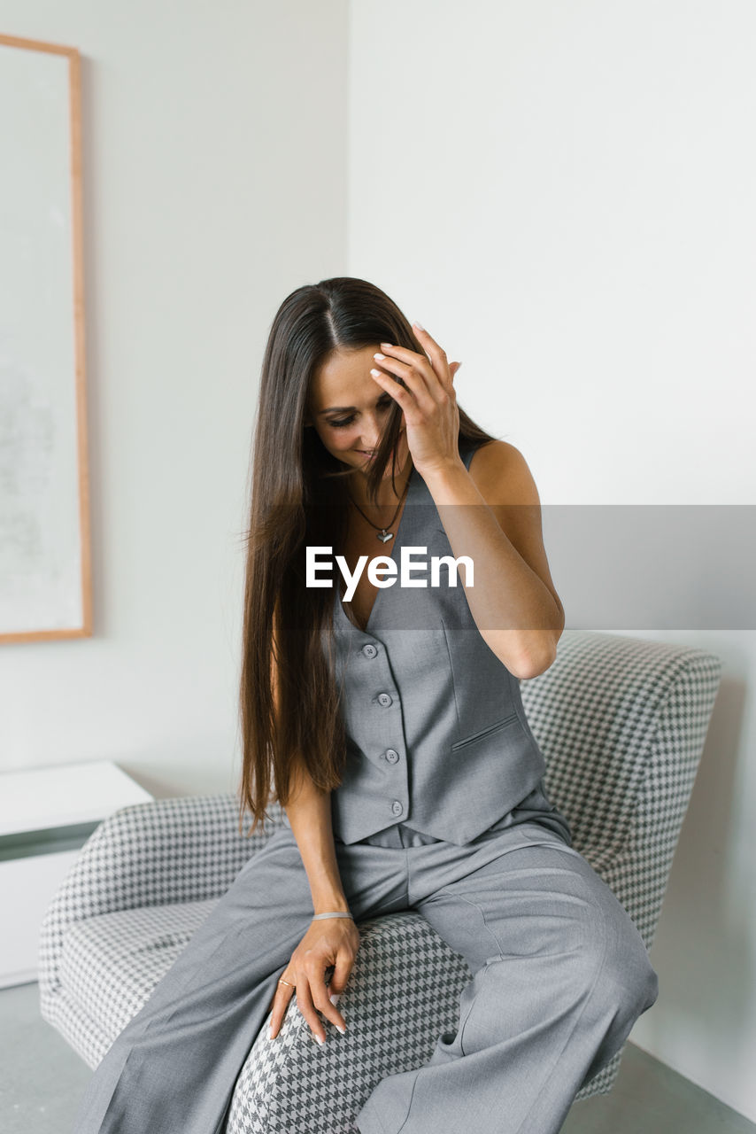 Happy woman in a gray vest and pants sits on a chair