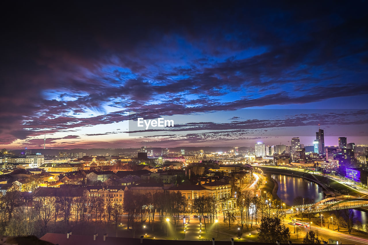 Illuminated city by river against sky at night