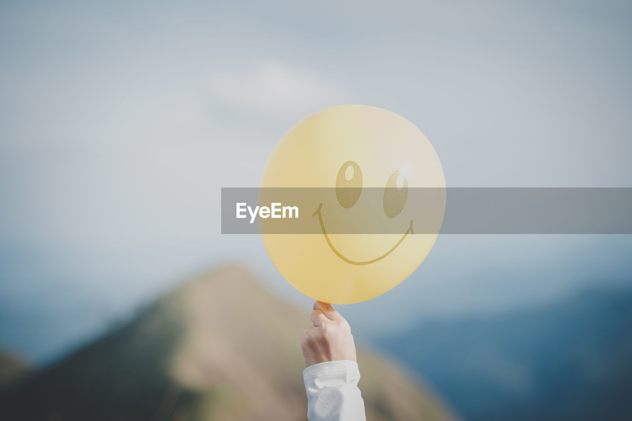 Hand holding a yellow balloon with a bright smiley face