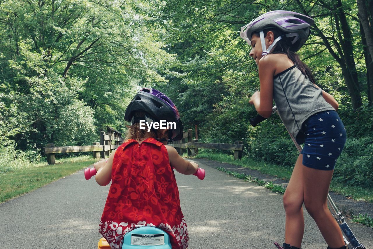 Rear view of girl on push scooter by sister cycling toy bicycle over footpath