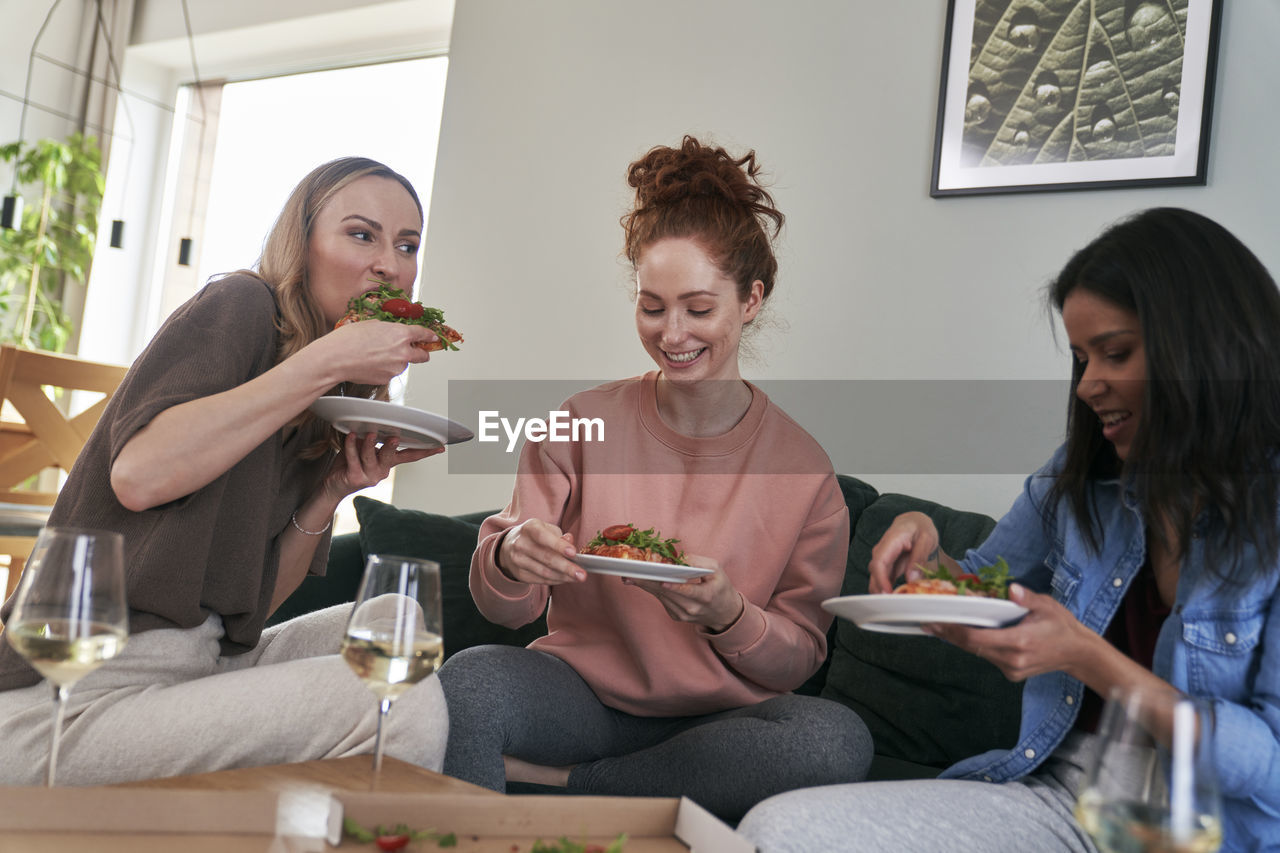 Cheerful female friends eating food at home