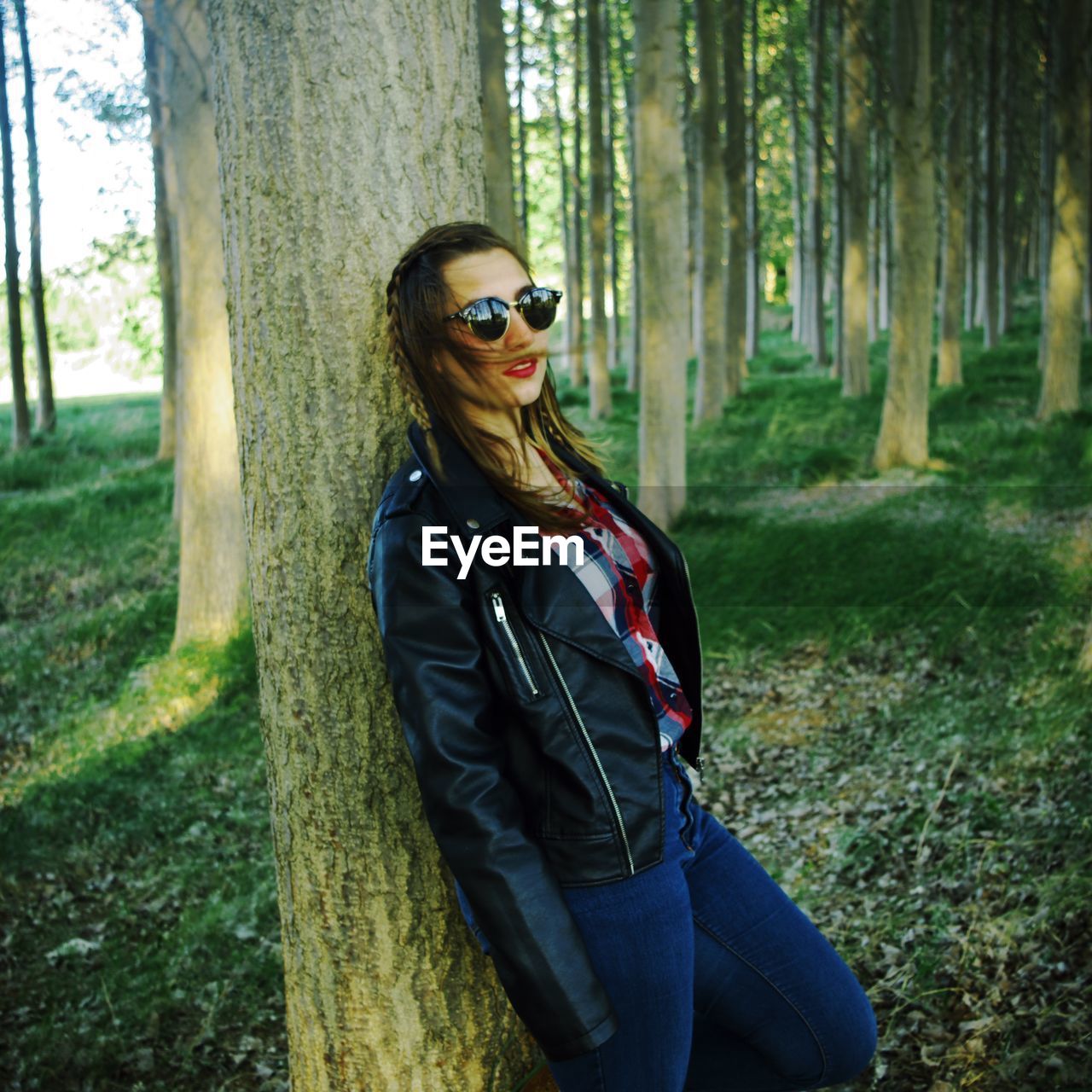 Portrait of woman wearing sunglasses while leaning on tree at forest