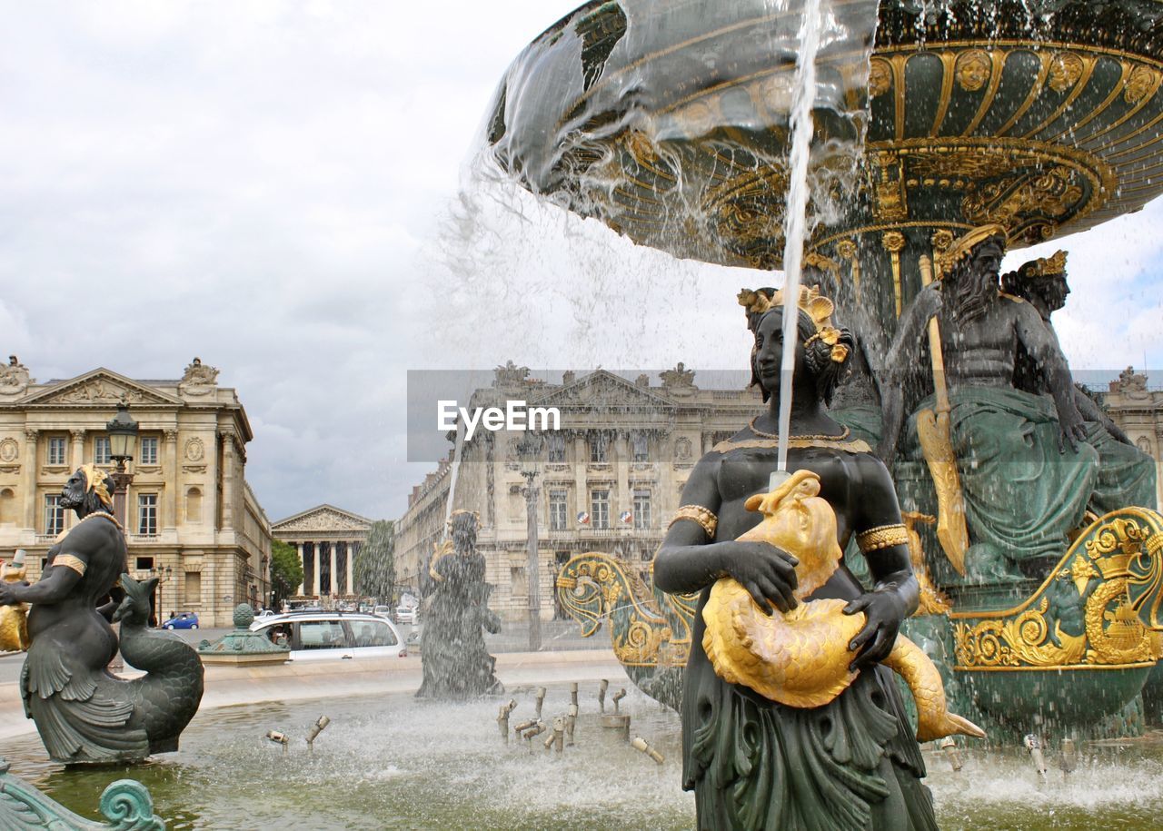 Statue by fountain in city against sky