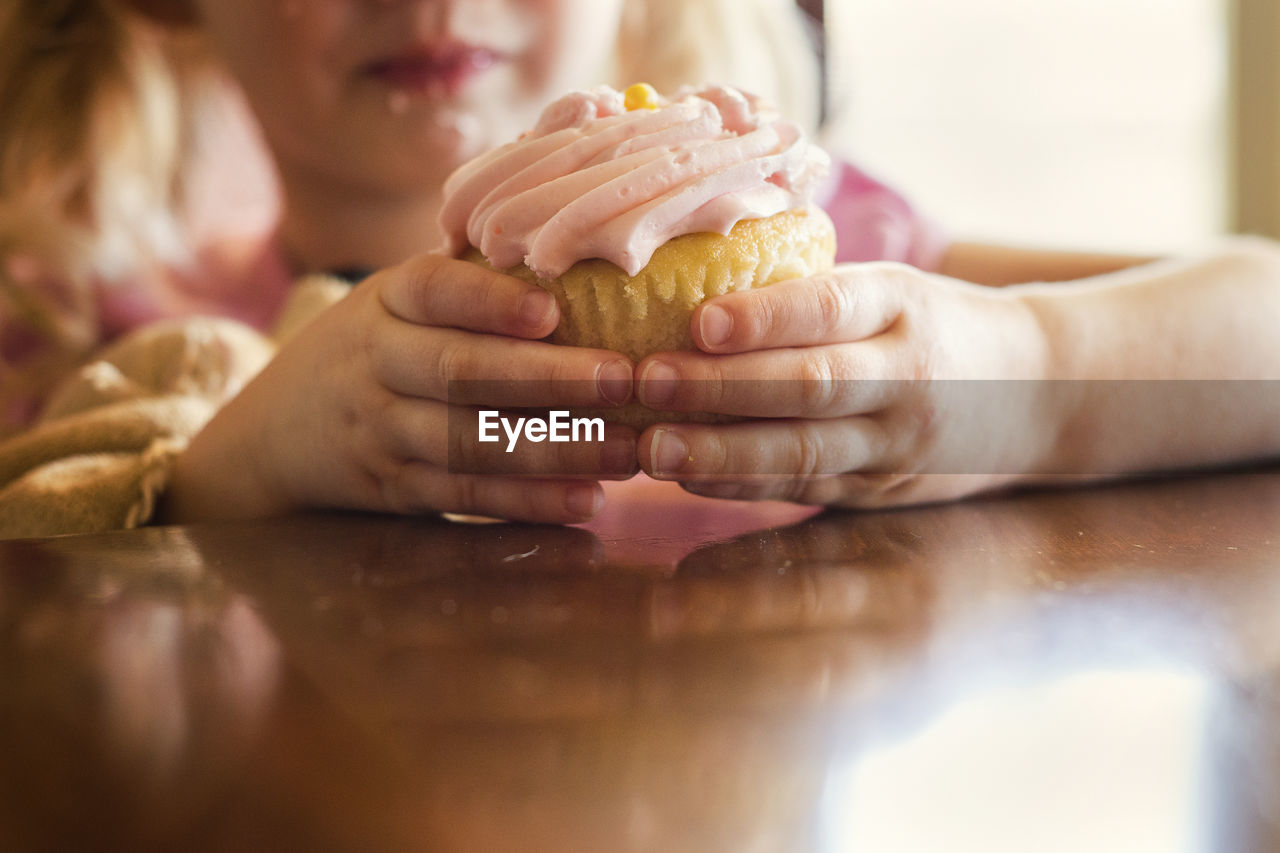 Midsection of girl holding cupcake at table in house