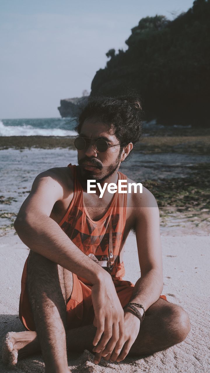 YOUNG MAN SITTING AT BEACH