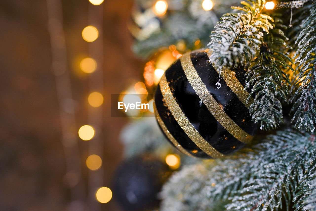 Gold and black christmas ornament hanging on the tree with blurred background