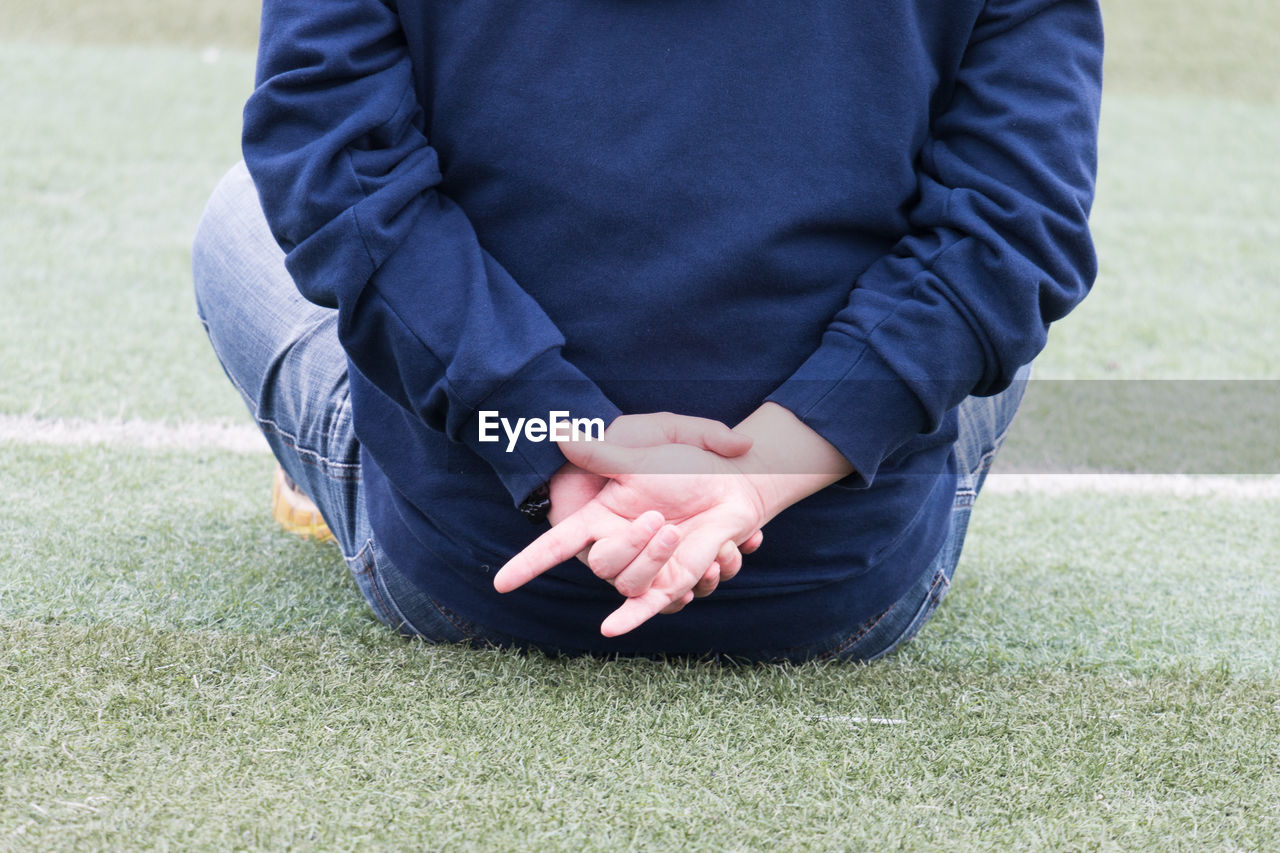Rear view of man showing horn sign while sitting on field