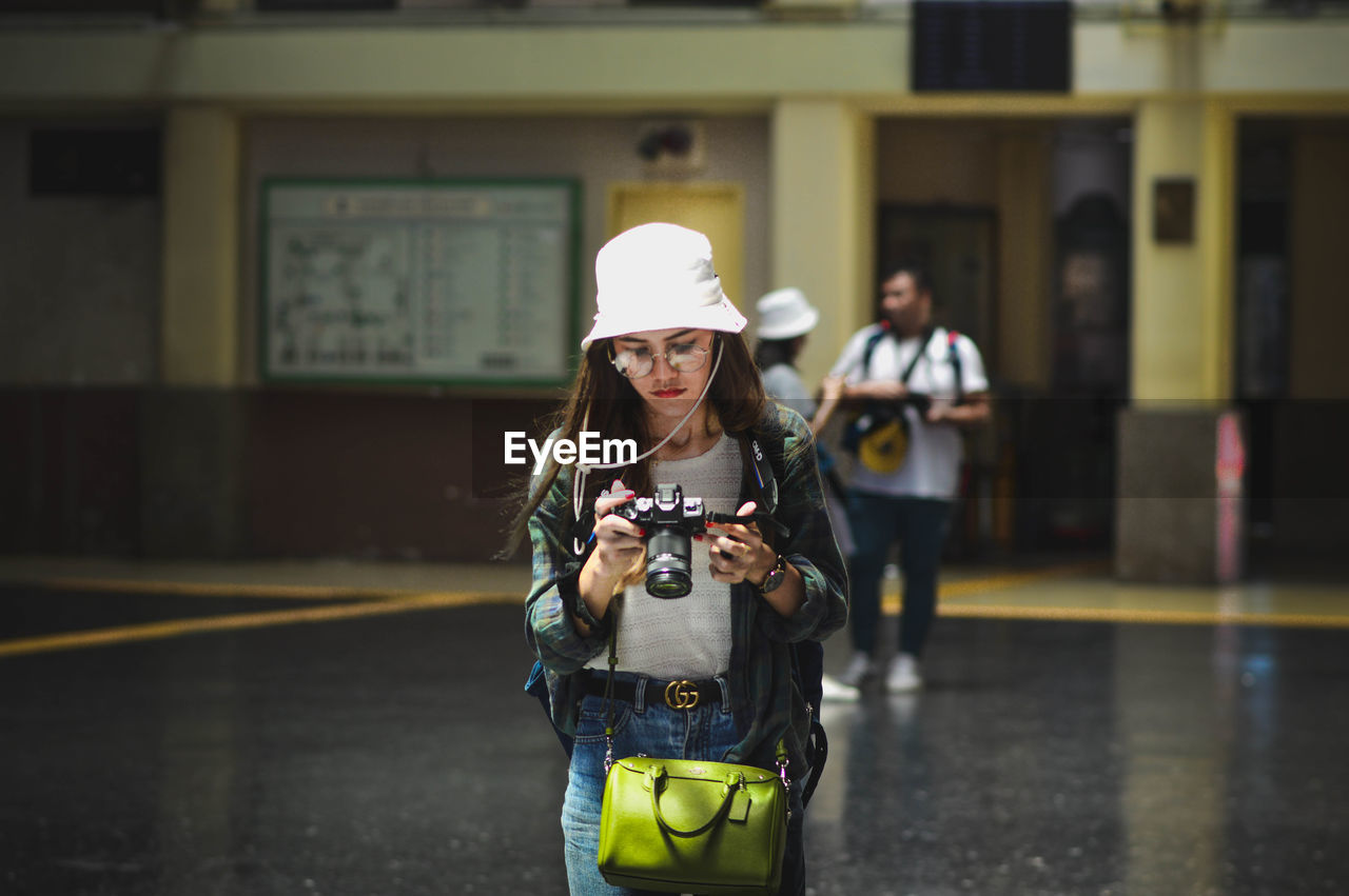 MAN HOLDING CAMERA WHILE STANDING AGAINST CITY