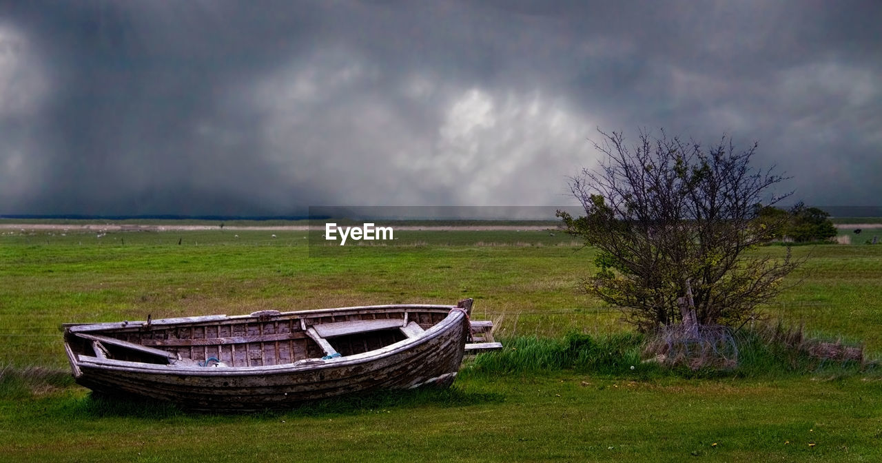 ABANDONED BOAT ON GRASS AGAINST SKY