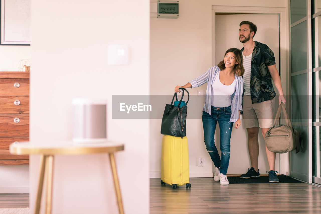 Full length of couple with luggage looking around in apartment while standing at doorway