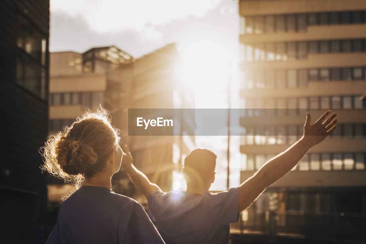 Rear view of doctor standing with arms outstretched by colleague on sunny day